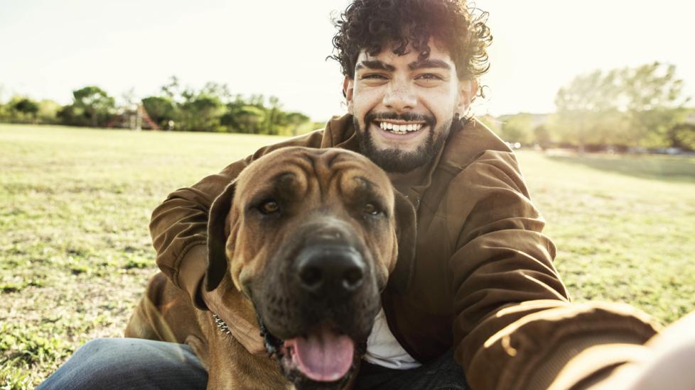 man-sitting-in-grass-with-dog-taking-selfie