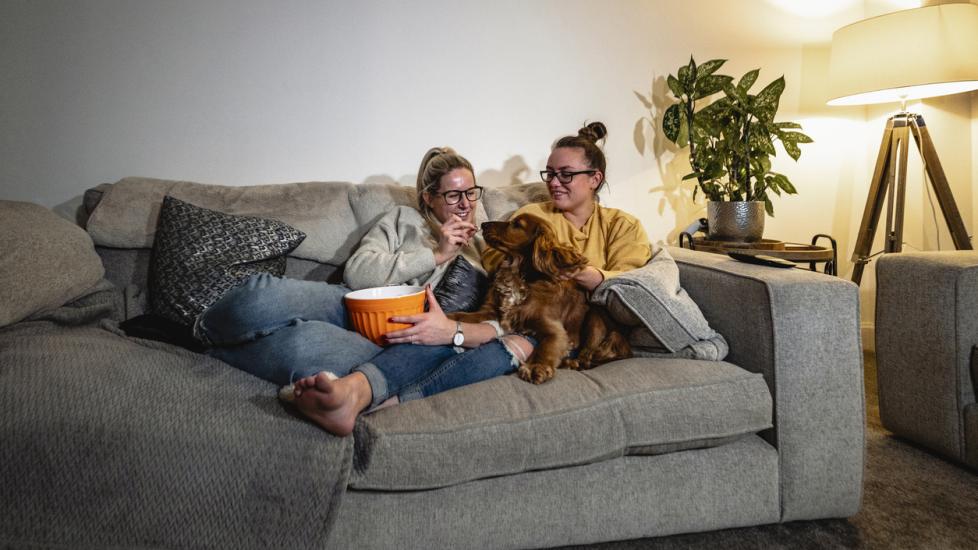 two girls cuddling on the couch with a dog and eating popcorn
