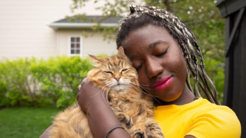 african american woman with eyes closed holds longhaired brown cat close to her cheek