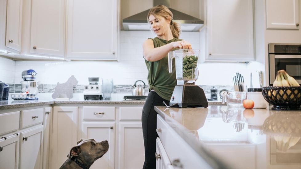 woman blending leafy greens while her dog watches