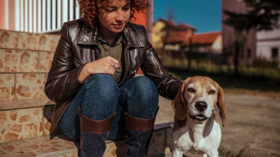 woman with curly hair and leather jacket pets beagle while sitting on steps outside building