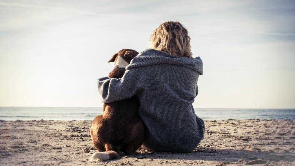 blonde woman sitting on beach hugging dog.