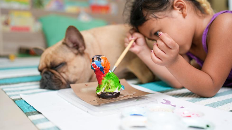 A little girl paints beside her dog.