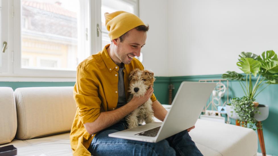 man sitting on couch with dog looking at laptop