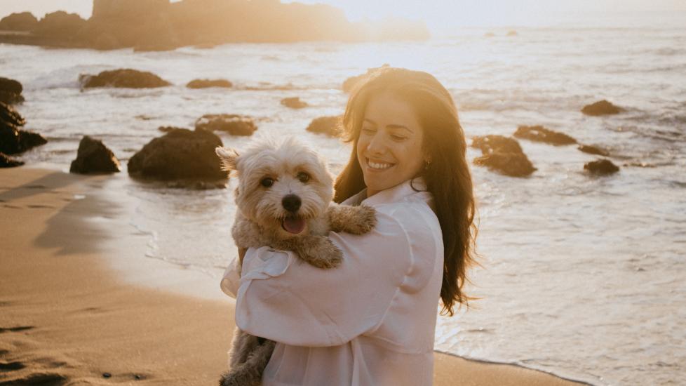 A woman holds her pup on the beach.