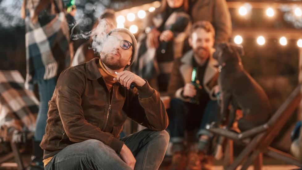 A man smokes beside a party with a dog.