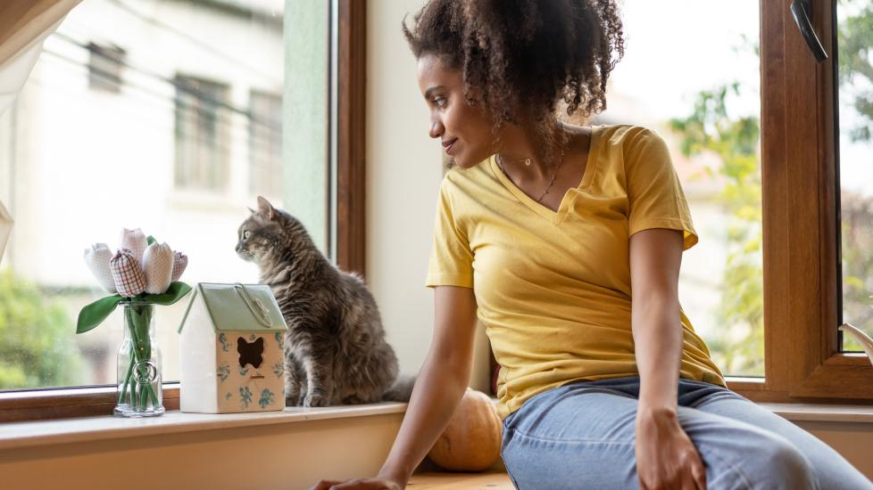 woman sitting with her gray tabby cat and looking out a window