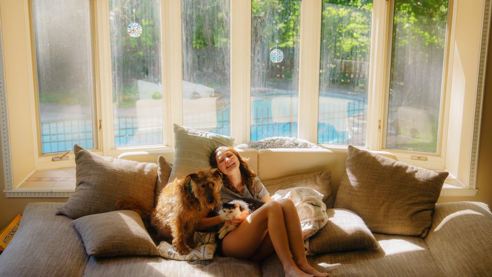 woman experiences the human-animal bond through cuddling her dog and cat.