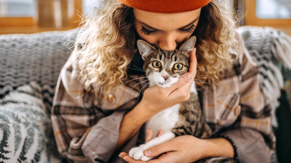 woman holds cat closely while sitting on the couch.